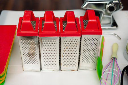 Stainless steel grater on the table on the kitchen table. Set of cooking utensils, whisk, acrylic spatula.の写真素材