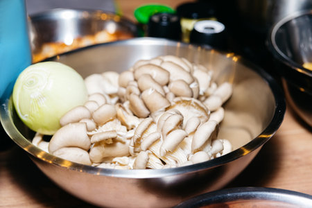 Oyster mushrooms in a metal bowl on a wooden table with peeled onion. Raw ingredients before cooking.の写真素材