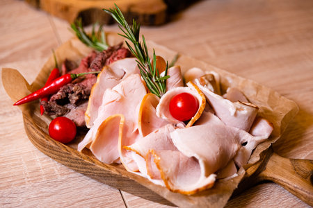 Sliced meat on a wooden board with rosemary and cherry tomatoes