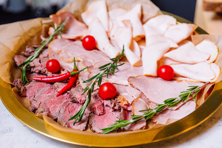 A delectable thin-sliced meats, including beef and pork sausages, ham, and rosemary red pepper delicacies. Accompanied by fresh cherry tomatoesの写真素材