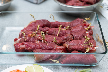 Raw beef meat rolls with spices and herbs in a glass tray on the tableの写真素材