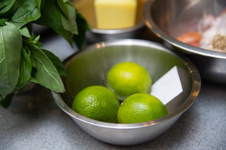 Ingredients for making sauce - lime, basil and butter. a metal bowl filled with limes on top of a counter.の写真素材
