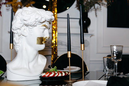 White marble bust of a man next to a glass of wine and black candles on the table. Luxurious restaurant interior.の写真素材