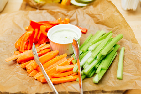 a wooden cutting board topped with sticks of carrots and celery with sauce on paper on the catering table. vegetables as an essential part of a balanced diet.の写真素材