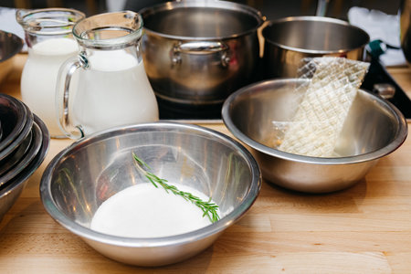 set of products for preparing panna cotta dessert: dry gelatin sheet, sugar, jugs of milk and cream, stainless steel bowls and pansの写真素材