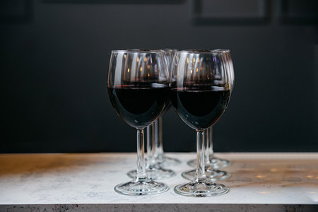 Two glasses of wine sitting on top of a bar counter top, dark grey backdrop