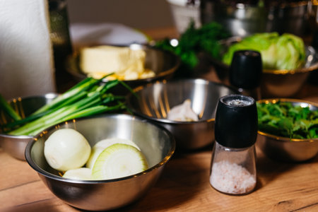 Cooking scene showcasing stainless steel bowls with onions and greens, alongside salt and pepper shakers on a wooden surface.の写真素材
