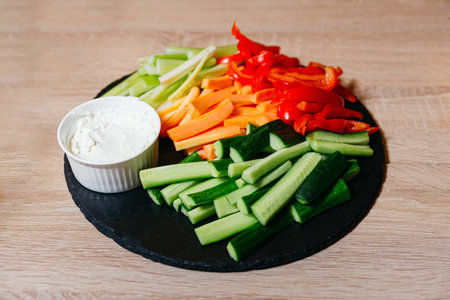 A black slate board adorned with vegetable sticks and a side of sour cream dip. A Colorful Delight:...