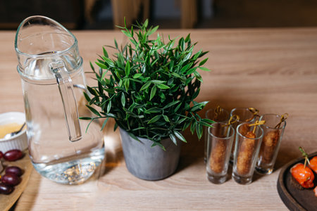 A contemporary glass water pitcher beside a lush green potted plant on a wooden table, creating a clean and refreshing ambiance.の写真素材