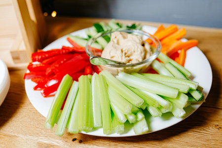 Colorful vegetable snack platter with fresh celery sticks, carrot sticks, red bell pepper, and...