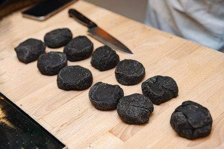 The dough with cuttlefish ink, is shaped into buns on a wooden chopping board, next to a chef's knife, indicating culinary preparation.の写真素材