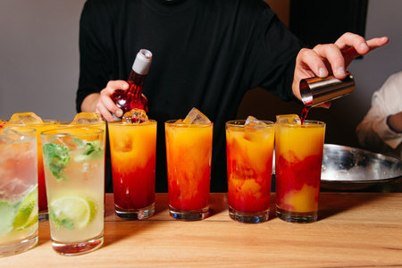 A bartender skillfully adding a red liqueur to layered cocktails with orange juice and ice, creating...
