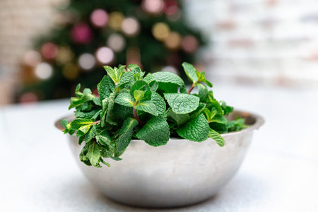 A bowl full of vibrant fresh mint leaves, ready to be used for culinary purposes or as a garnish, with festive background.の写真素材