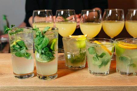 A variety of citrus cocktails with fresh mint, ice, and slices of lime and orange on a bar counter.