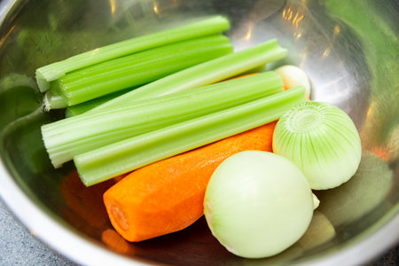 Celery, carrot, and onion, the classic mirepoix ingredients, arranged in a stainless steel bowl for meal preparation.の写真素材