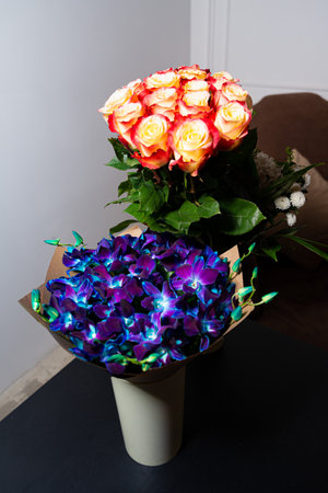 A stunning bouquet of fresh, bright roses and exotic blue orchids arranged in a vase, perfect for a gift or decoration.の写真素材