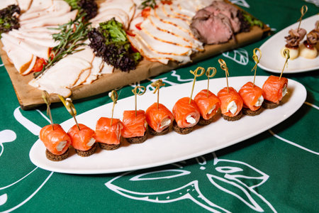 Smoked salmon rolls with cream cheese on pumpernickel bread, elegantly presented on a white serving platter for an event.の写真素材