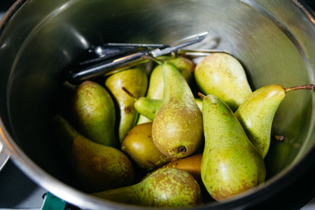Ripe green pears in a metal bowl with peeler, ready for cooking, emphasizing freshness and organic produce.の写真素材