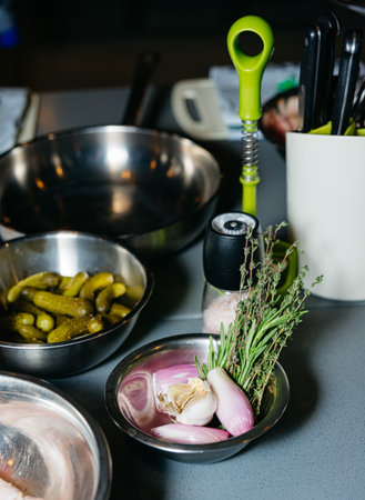 Cooking preparation area with fresh shallots, garlic, and thyme in stainless steel bowls, alongside...