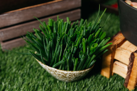 A wicker basket filled with fresh chives displayed on artificial grass, with wooden crates in the...