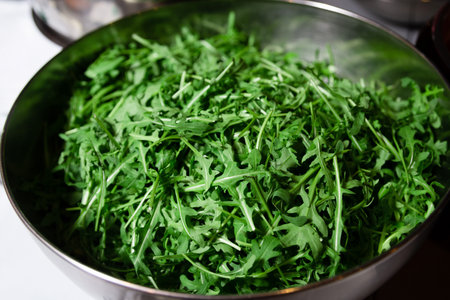 A bowl full of vibrant green arugula leaves, freshly washed and ready for salad preparation.の写真素材