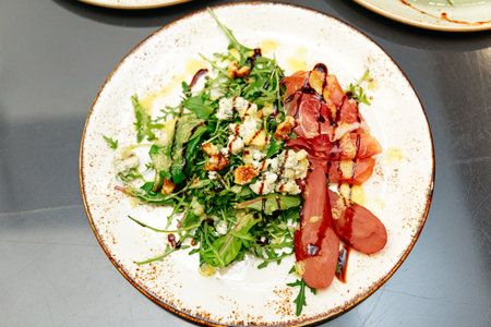 A beautifully plated arugula salad with poached pears, prosciutto, blue cheese, candied walnuts, balsamic glaze, and dressing, served on a rustic ceramic plate.の写真素材