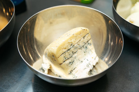 A creamy wedge of blue cheese with marbled veins of mold, placed in a stainless steel bowl, ready for cooking, tasting, or serving.の写真素材