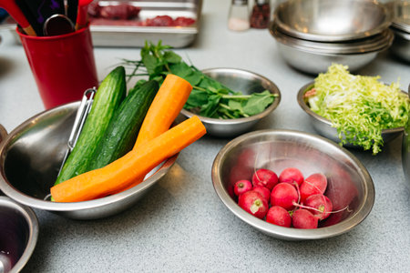 Assorted fresh vegetables including carrots, cucumbers, radishes, and greens arranged in metal bowls...