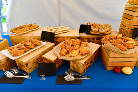 Beautifully arranged catering display featuring croissant sandwiches, mini wraps, and finger foods on wooden crates and a blue tablecloth.の写真素材
