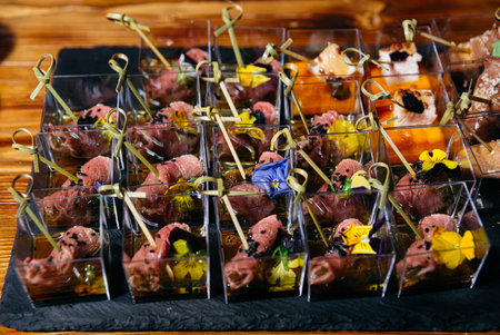 Gourmet beef tartare served in individual cups, garnished with edible flowers, black sesame seeds,...