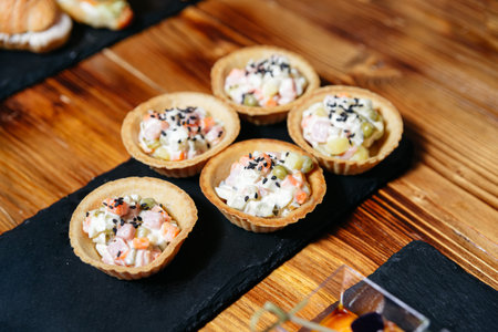Bite-sized tartlets filled with creamy vegetable salad, garnished with black sesame seeds, arranged...