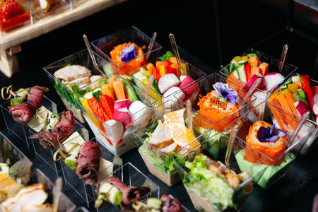 An assorted display of elegant bite-sized appetizers in clear cups, featuring vegetables, meat rolls, mousse, and edible flowers.の写真素材