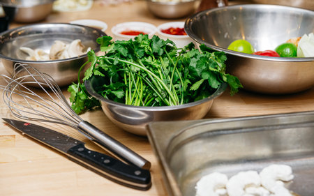 Bowl of fresh cilantro on a kitchen counter with a whisk, knife, and other cooking ingredients prepared for a recipe.の写真素材