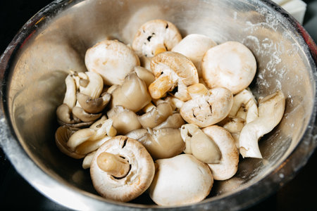Close-up view of fresh mixed mushrooms including button and oyster types, placed in a stainless steel bowl for cooking preparation.の写真素材