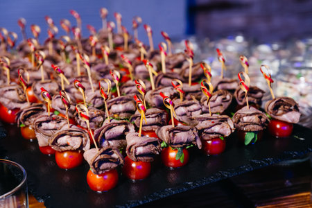 Elegant hors d'oeuvres featuring rolled roast beef on cherry tomatoes with skewers, ideal for catering or cocktail parties.の写真素材