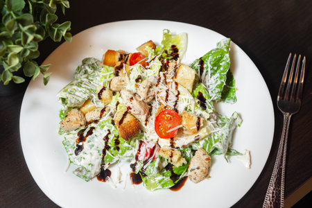 A classic Caesar salad with grilled chicken, romaine lettuce, cherry tomatoes, croutons, Parmesan cheese, and creamy dressing on a white plate.の写真素材