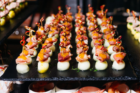 Elegant skewers featuring prosciutto-wrapped melon balls topped with mango or apricot sauce, served...