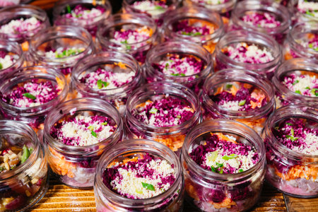 Brightly colored beetroot and carrot layered salads topped with crumbled cheese, served in small glass jars for catering events.の写真素材