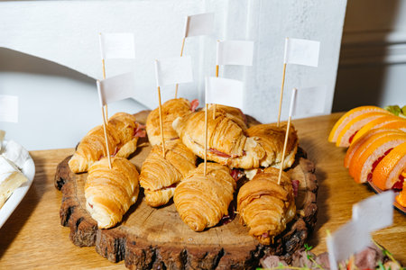 Golden croissant sandwiches filled with deli meat, arranged on a wooden platter for a catering event or breakfast buffet.の写真素材