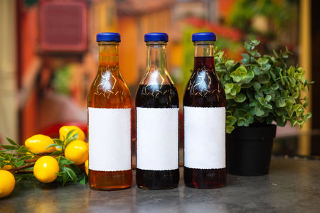 Three glass bottles with blank white labels and blue caps, containing different colored liquids,...