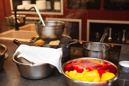 Busy kitchen scene showing steaming pots, stainless steel bowls, and colorful red and yellow bell peppers ready for cooking.の写真素材