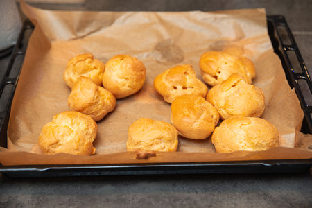 Golden brown cream puffs resting on baking paper after being freshly baked, ready to be filled with sweet or savory fillings.の写真素材