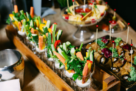 Colorful fresh vegetable sticks served upright in small glasses with a creamy dip, ideal for parties, catering, and healthy snacking.の写真素材