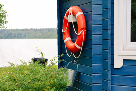 Orange lifebuoy with rope mounted on a blue wooden wall near a calm lake, used for water safety and emergency rescue.の写真素材