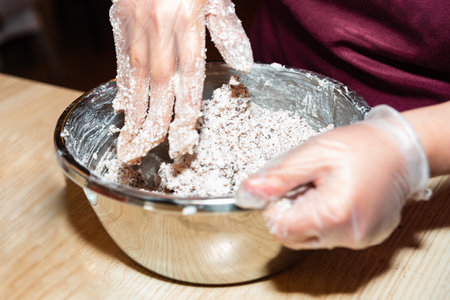Close-up of a person wearing gloves while mixing flour and cocoa mixture into dough inside a...