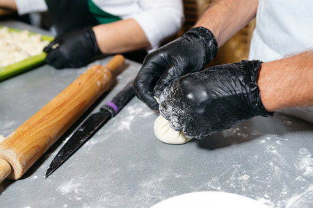 Close-up of hands folding dough to make dumplings, with rolling pin and knife on countertop in kitchen.の写真素材