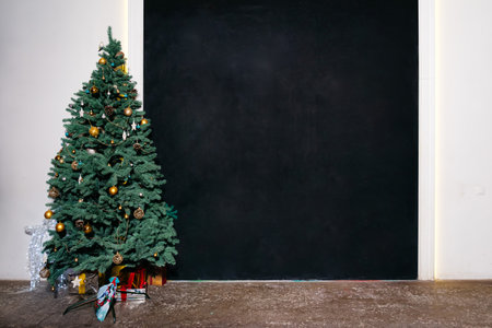 Beautiful Christmas tree with gold ornaments and presents underneath, placed in a minimalist room with a black wall backdrop.の写真素材