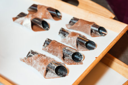 Unbaked chocolate pastry shells are wrapped around metal molds, placed on a tray ready for oven baking preparation.の写真素材
