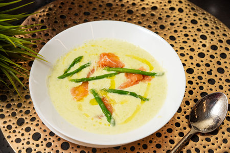 Gourmet bowl of creamy asparagus soup garnished with green asparagus spears, smoked salmon slices, and olive oil drizzle.の写真素材