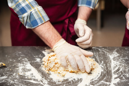 Close-up of gloved hands kneading fresh pasta dough on a floured countertop during a cooking class...